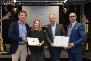 Lehrlingsportal.at Vier Personen in Geschäftskleidung stehen auf einer Bühne und halten Kisten; eine Kiste trägt ein Apple-Logo. Im Hintergrund sind Bühnenbeleuchtung und eine dekorative kreisförmige Projektion zu sehen.